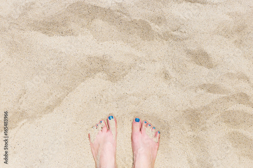 Young woman's foots with blue pedicure on the yellow sand