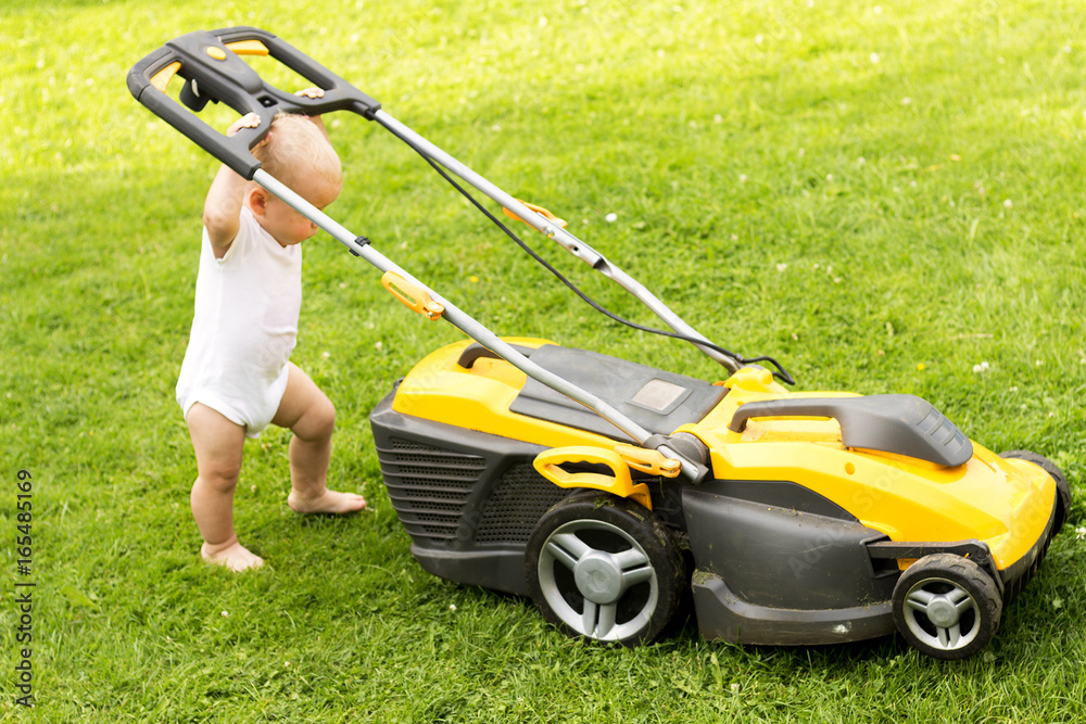 Funny baby boy cuts the lawn with a grassmower Funny baby boy cuts the lawn with a grassmower