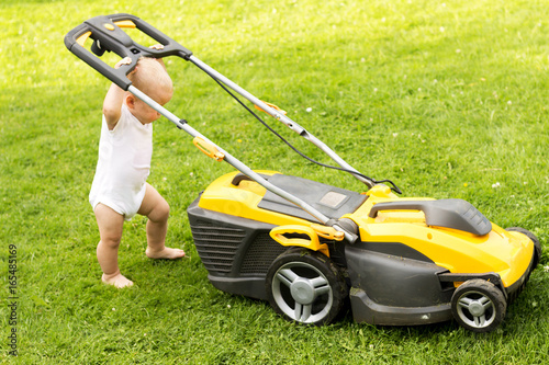 Funny baby boy cuts the lawn with a grassmower photo