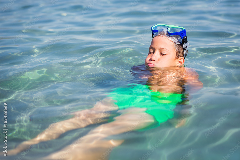 Young cute boy bathing and cooling in shallow seawater wearing scuba mask during summer vacation