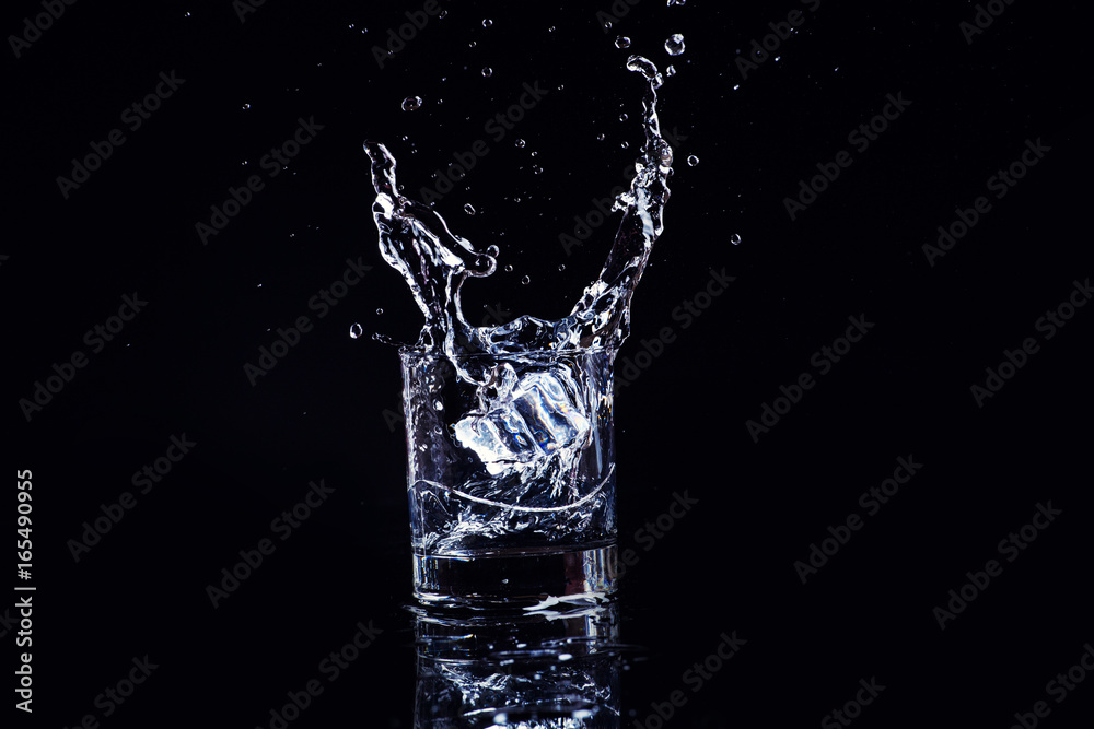 Isolated cold water in a glass with splash and cubes of ice on black background, brandy in a glass