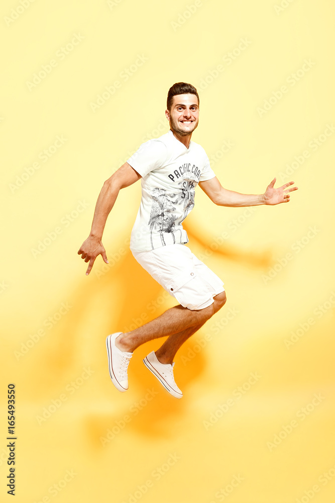 Shot of handsome bearded guy dressed in white t-shirt and shorts jumping looking at camera smiling.