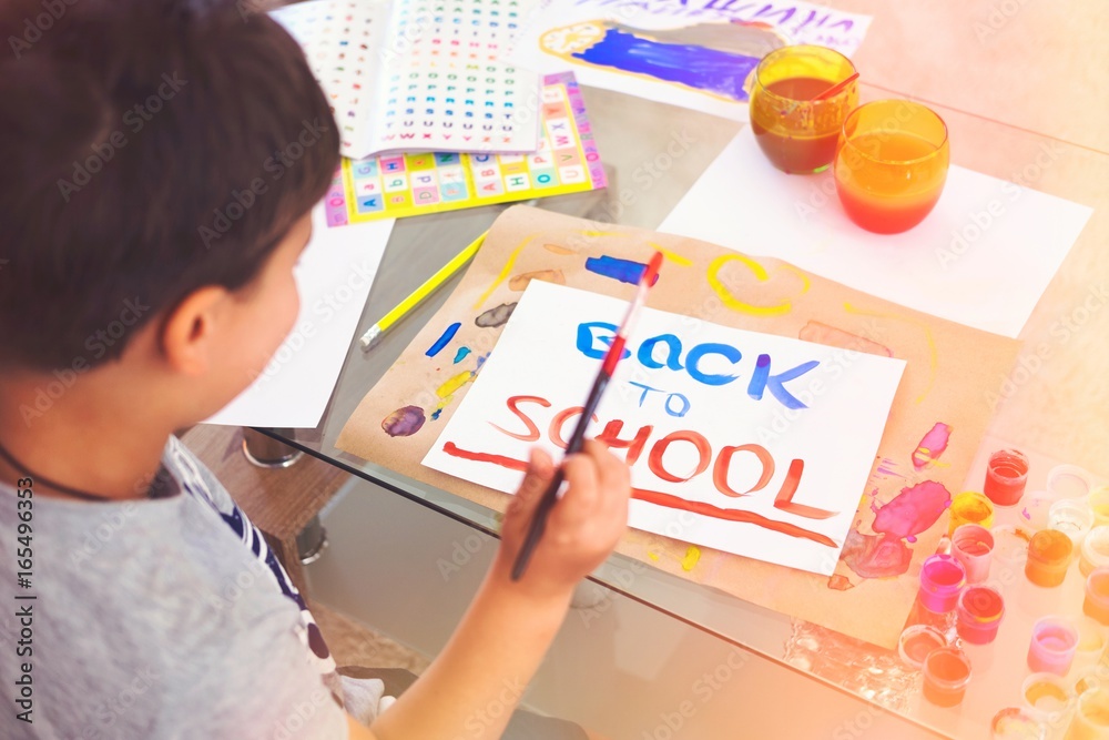 Young boy writing Back to schoolYoung boy painting Back to school text. Overhead shot. Toned