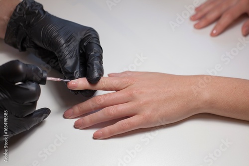 Manicurist black gloves doing a manicure at the beauty salon on a white background. Nail Polish colors Nude. Beautiful women's hands