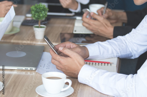 Businessman using smartphone at restaurant, writing an sms message via cellphone while sitting at modern cafe with team, flare light