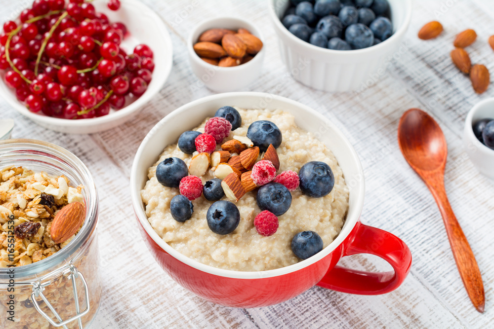 Oatmeal porridge bowl with blueberries, almonds and raspberries on white wooden table. Closeup view Healthy breakfast food
