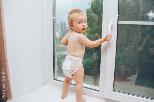 baby holding handle of window and looking at the street