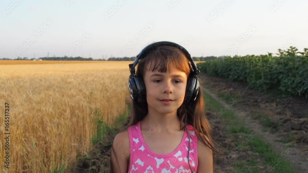 Child in the field wearing headphones. A little girl is listening to music in nature. Child in the field wearing headphones. A little girl is listening to music in nature.