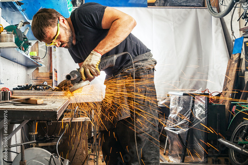 Fotografie A strong man with hard-working hands in work clothes brewing a metal welding mac