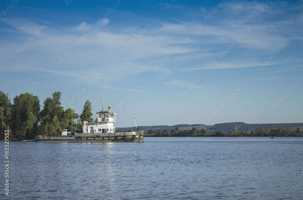 A Russian ship sails along the river under a blue sky with white clouds.