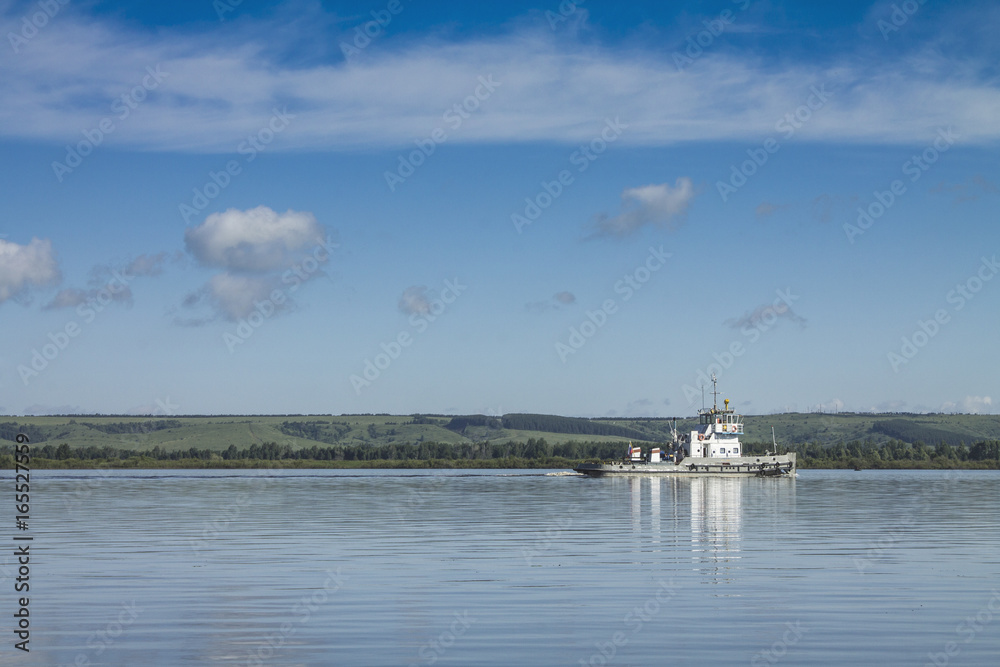 A Russian ship sails along the river under a blue sky with white clouds.