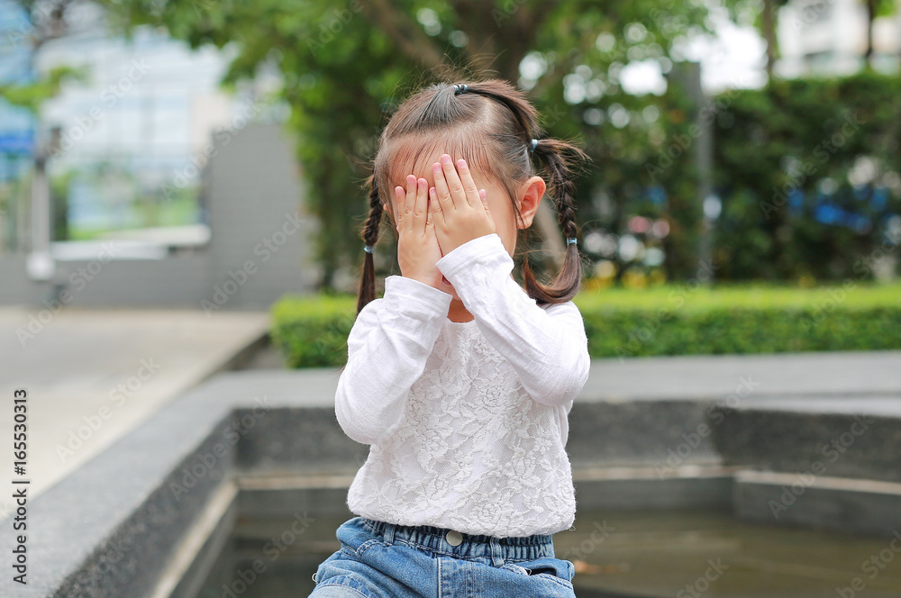 Asian little girl cover her face with her hands.