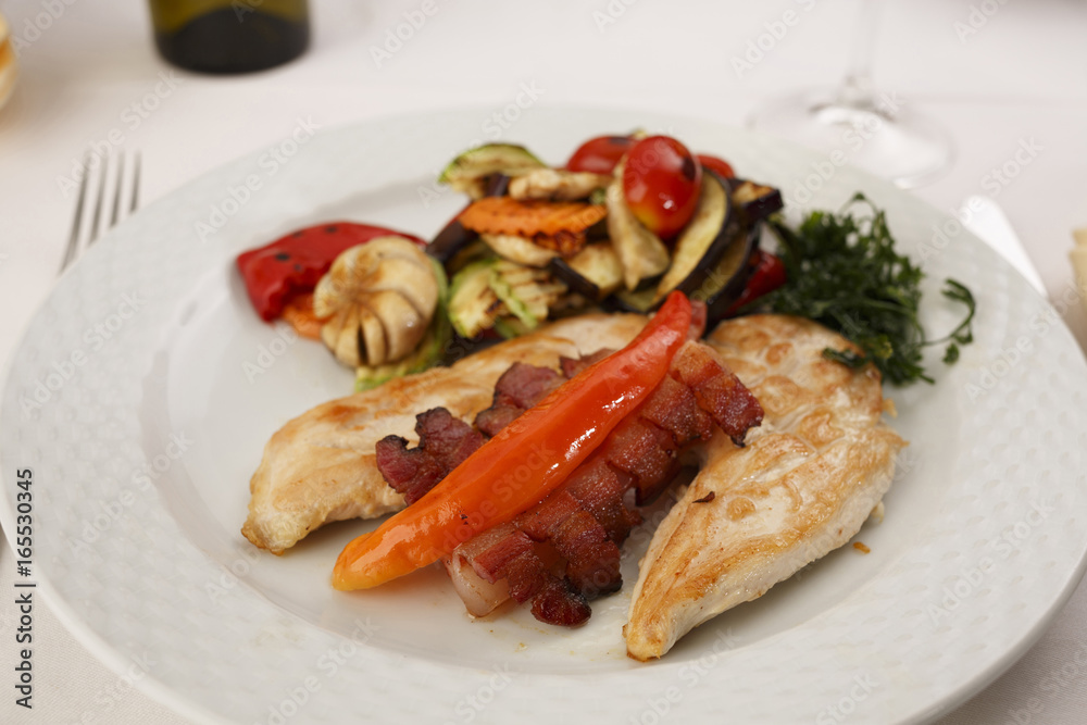 Chicken with bacon and grilled vegetables arranged on a plate, Traditional dish in elegant setting, Selective focus with soft light