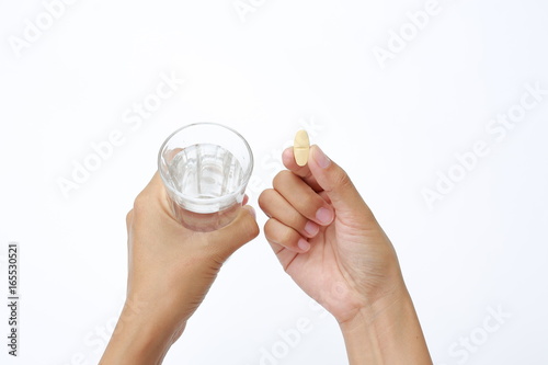 Photos Hand holding yellow pill with water in glass isolated on white background