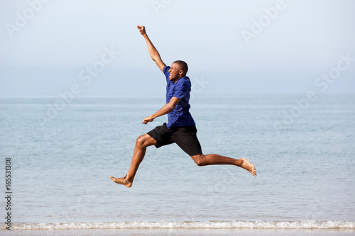 Portrait of excited young african guy running and jumping along the sea