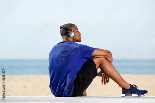 Fit african man listening to music at beach © mimagephotos