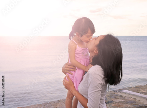 mother and kid girl kissing with natural emotion smiling on sea background in the evening. © zilvergolf