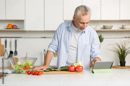 Handsome mature man standing at the kitchen cooking salad.