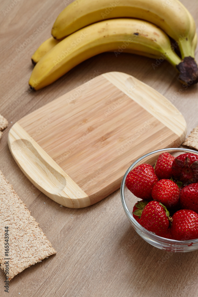 Fruit on the table. View from above. Healthy food. On a wooden table lie strawberries, bananas, bread and milk in a glass. Wooden board for text. Fruit on the table. View from above. Healthy food. On a wooden table lie strawberries, bananas, bread and milk in a glass. Wooden board for text.