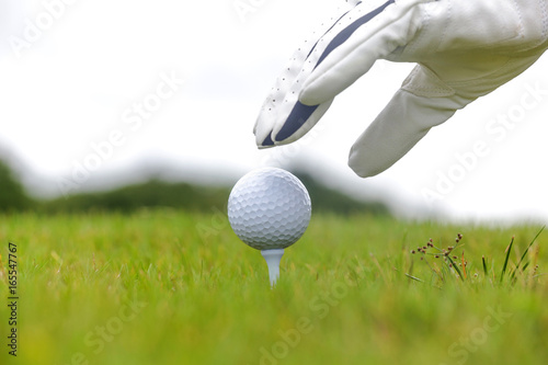 Hand holding golf ball with tee on golf course