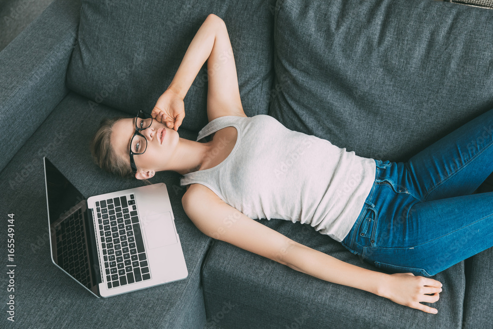 Naklejka premium Young attractive blonde woman resting near laptop on sofa in living room