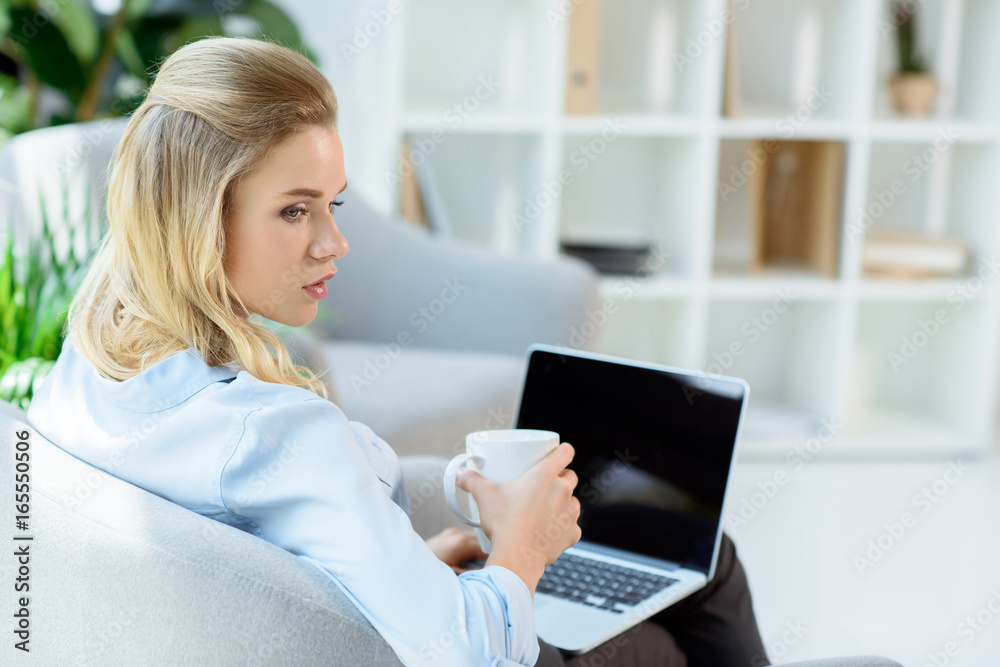 back view of businesswoman with cup of coffee and laptop sitting in armchair back view of businesswoman with cup of coffee and laptop sitting in armchair