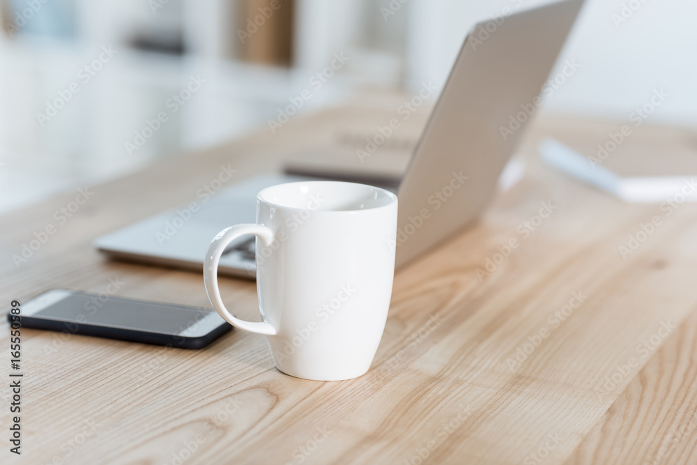 selective focus of coffee cup standing on table with digital devices in office selective focus of coffee cup standing on table with digital devices in office