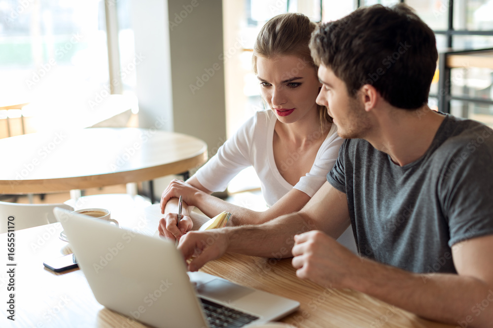 young couple working on laptop together while sitting at table in cafe young couple working on laptop together while sitting at table in cafe
