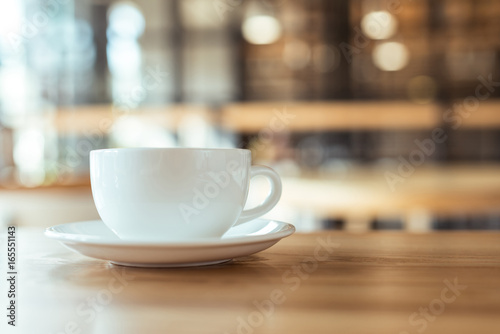 close up view of cup of coffee on saucer on wooden table in coffee shop