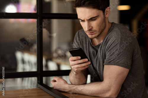 young focused man using digital smartphone while sitting in cafe