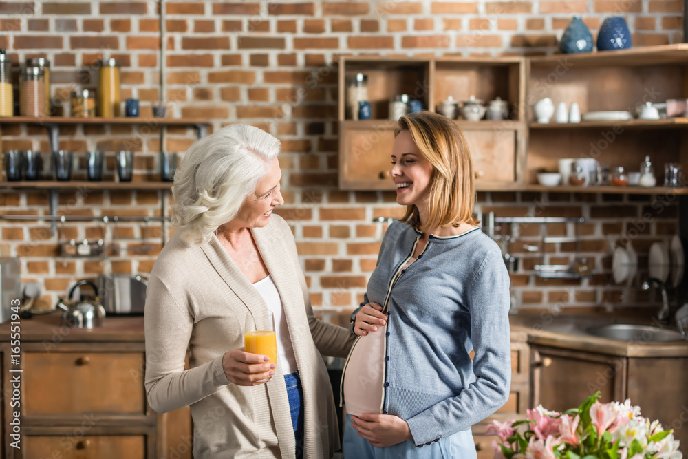 Portrait of young pregnant woman and her senior mother on kitchen