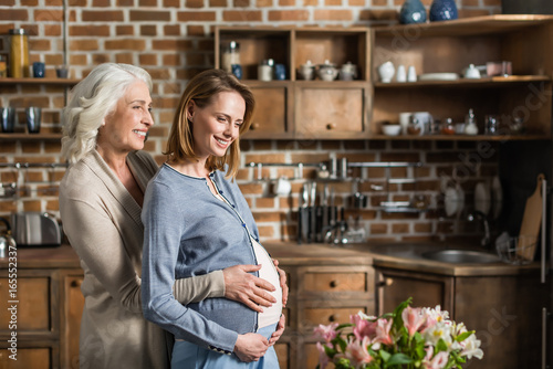 Portrait of young pregnant woman and her senior mother on kitchen