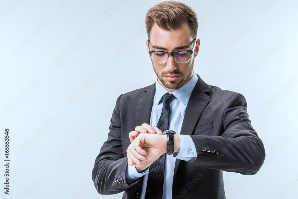 portrait of young businessman in eyeglasses checking time on watch isolated on blue