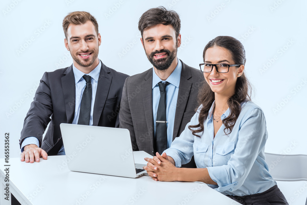 Fototapeta premium portrait of smiling business people looking at camera while sitting at workplace with laptop