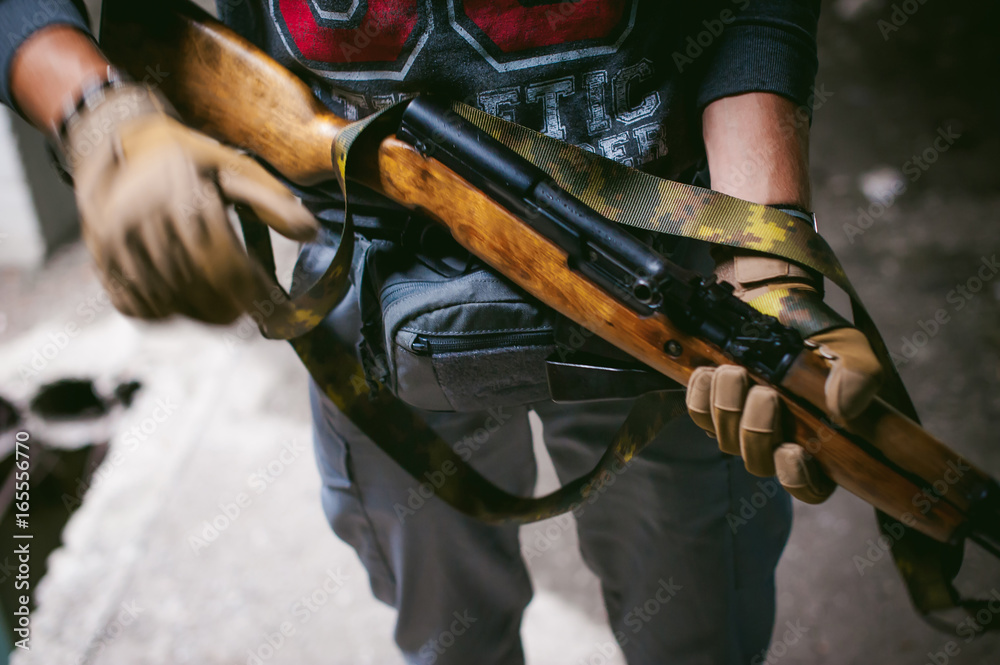 Fototapeta premium Athletic man in gray clothes with a carbine gun in his hand. Close-up of tactical gloves with weapons