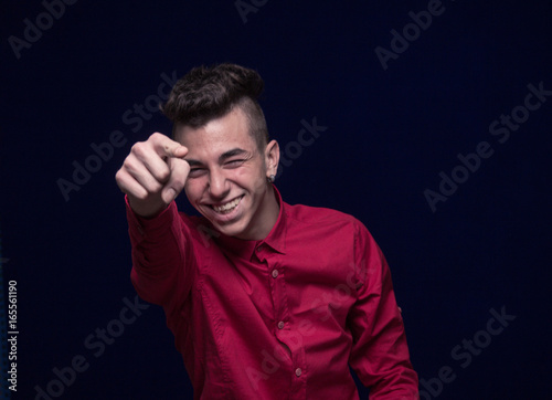 one teenager boy, red shirt, Caucasian, dark background, looking to camera, smiling, pointing finger to camera