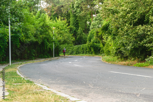 unrecognizable man walking on the road with green lush vegetation
