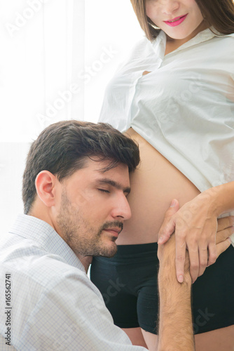 pregnant woman and her handsome husband is listening to baby in belly