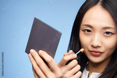 Beautiful young woman on blue background applies cosmetics, asian