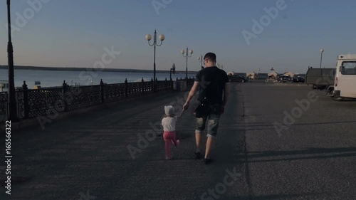 The father and his little daughter are holding hands along the embankment. Slow motion