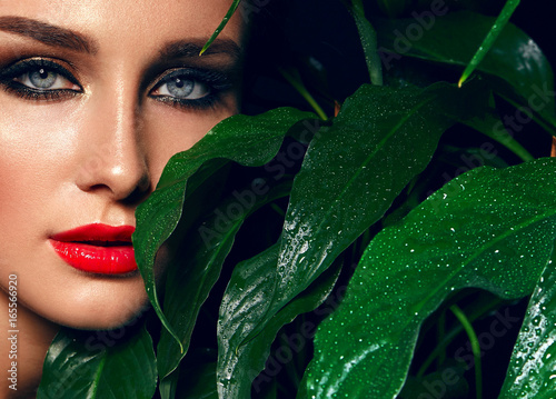 Beautiful sultry tanned girl with bright make-up and dark hair. She is in the jungle among the leaves. Cosmetics, spa, health, relaxation.