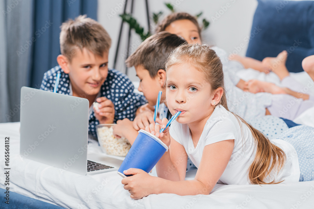 little girl drinking soda while friends using laptop at home