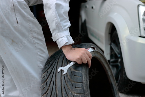 Selective focus on hands of car mechanic in uniform holding wrench and tire at the repair garage background.