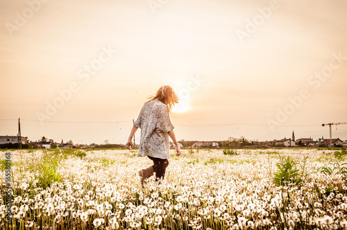 woman running free in dandelion field at sunset in summer day