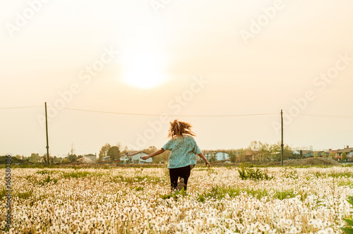 woman running free in dandelion field at sunset in summer day