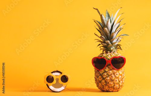 Pineapple and coconut wearing sunglasses on a bright yellow background