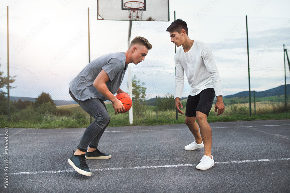 Fototapeta premium Handsome teenage boys playing basketball outdoors on playground.