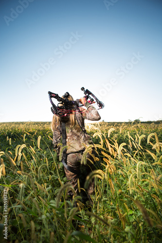 Hunter with bow walking through tall grass