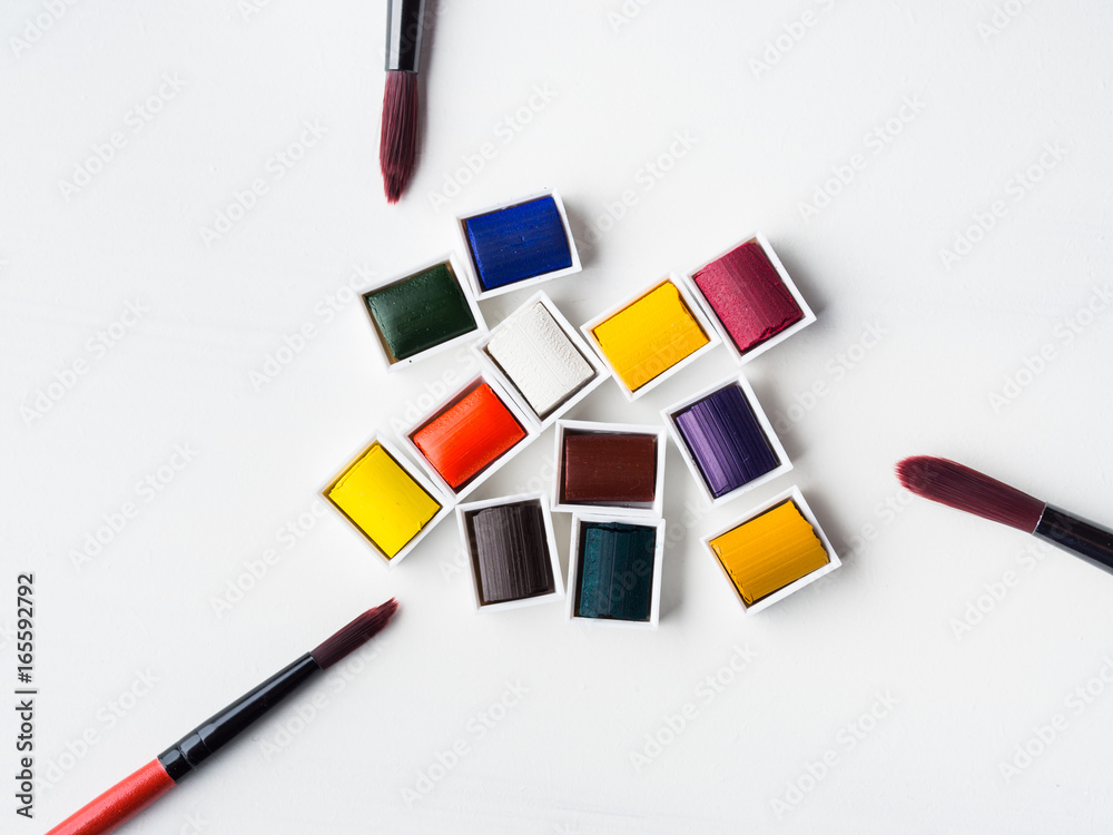 Fototapeta premium Watercolor godets and brushes on white background. Flat lay. Copy space