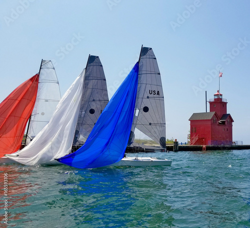 red white and blue spinnakers on sailboats in Holland Michigan harbor with red lighthouse 
